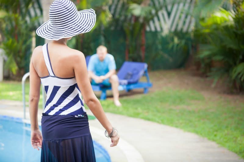 a woman wearing a navy swimsuit and summer hat