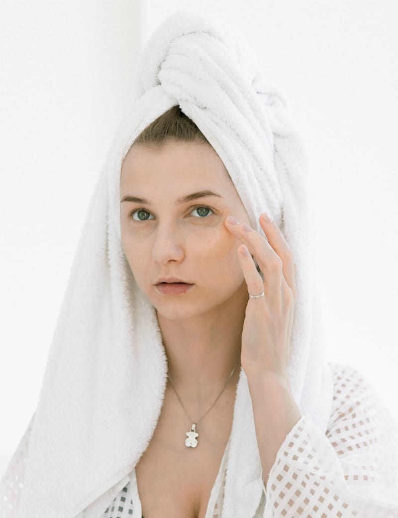 A woman with her hair in a white towel touching her face