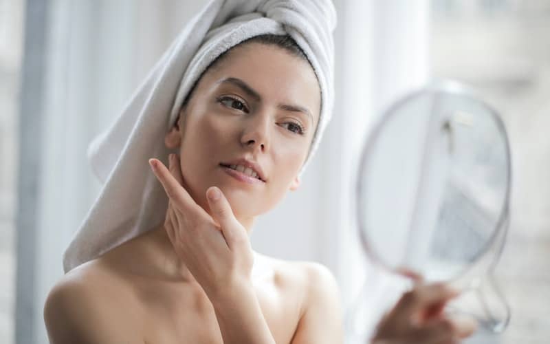 A woman applying Exuviance Matte Perfection to her face in the mirror