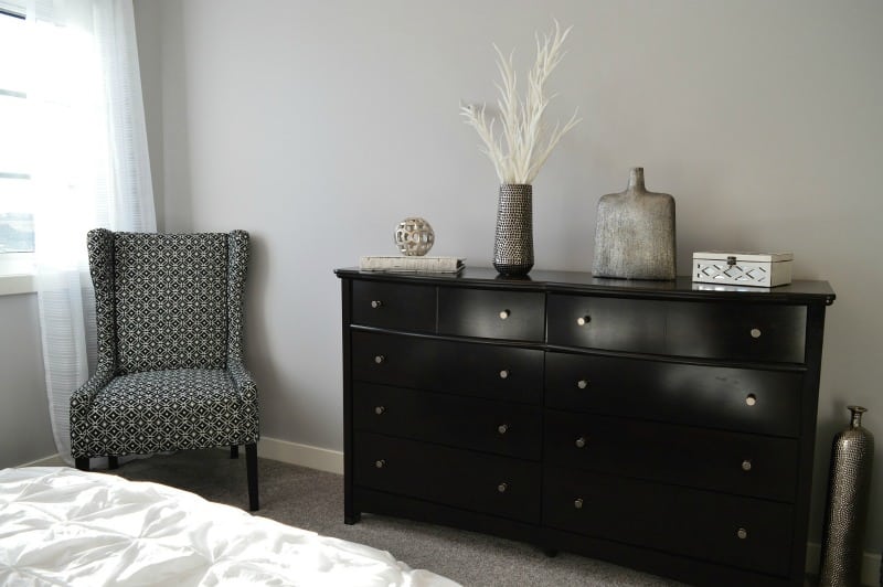 a relaxing bedroom with a bureau and chair