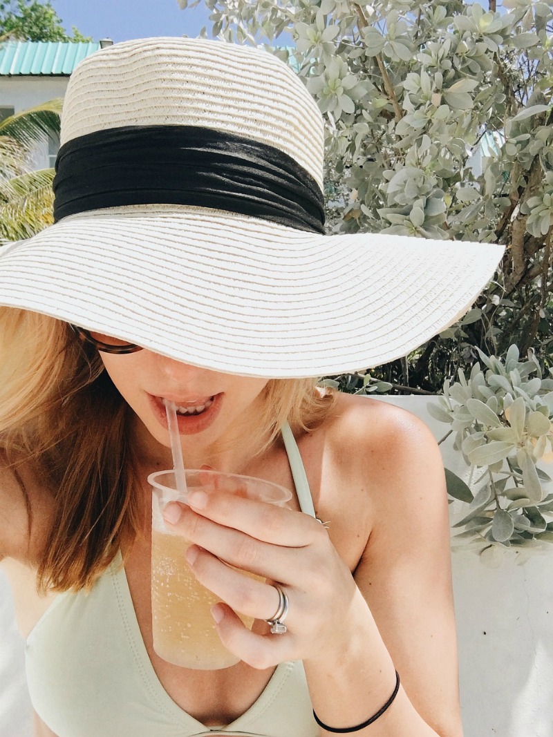 Woman wearing a floppy hat and sipping a cold drink following these summer sun safety tips