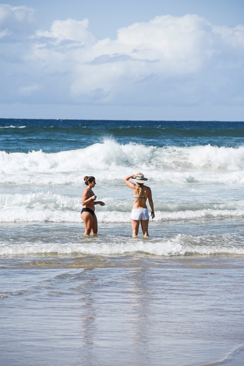 two mature women in bathing suits standing in the waves on the beach