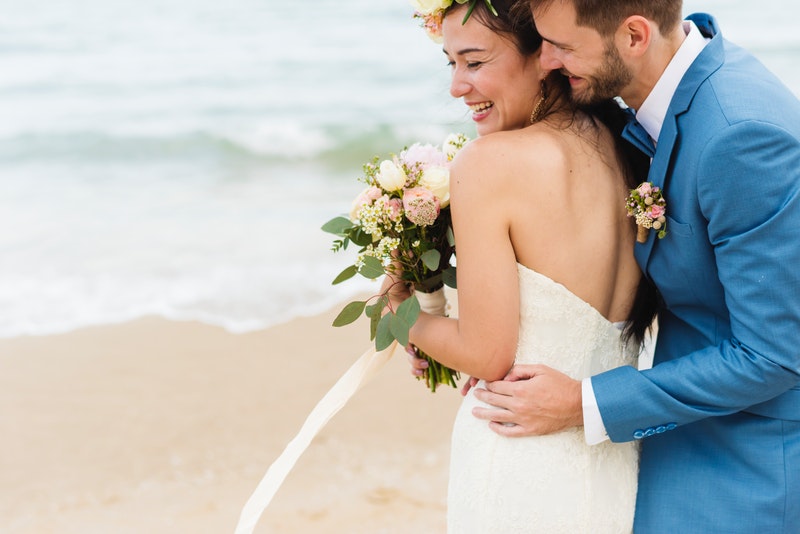 a bride and groom laughing on the beach