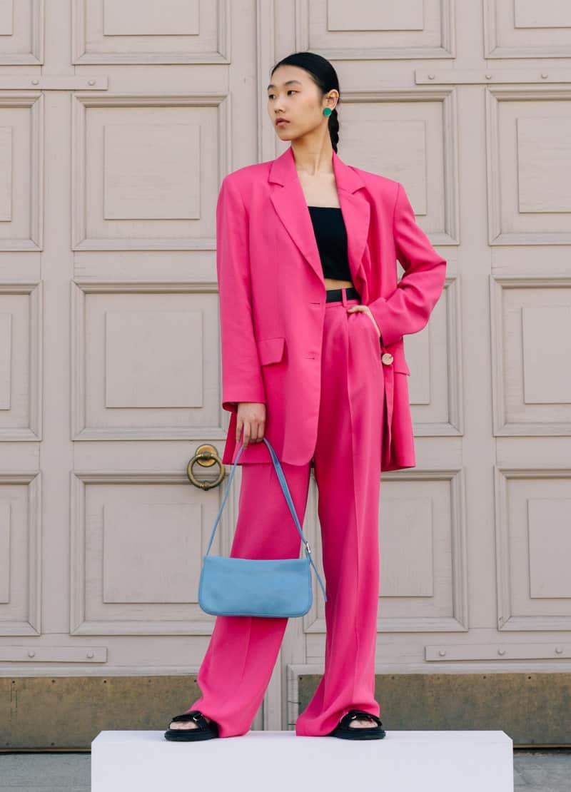 a woman wearing a pink suit and blue bag