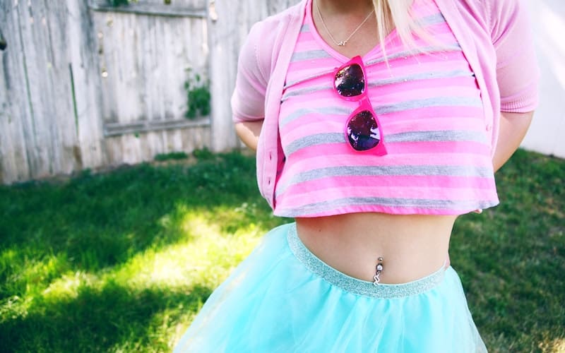 woman wearing a turquoise skirt and pink top with a pierced naval