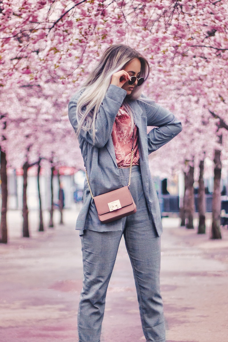 A stylish woman wearing grey in front of pink trees