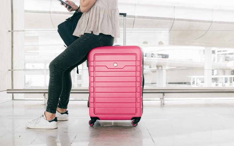a woman sitting on a pink suitcase looking through her bag