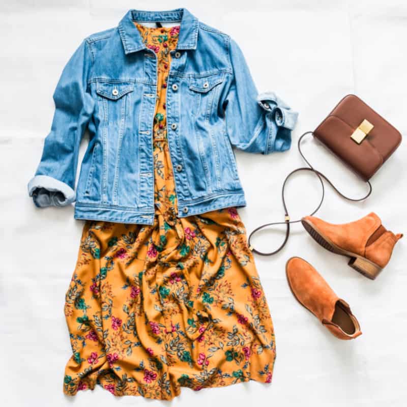 a flat lay of a denim jacket with a dress, boots and bag