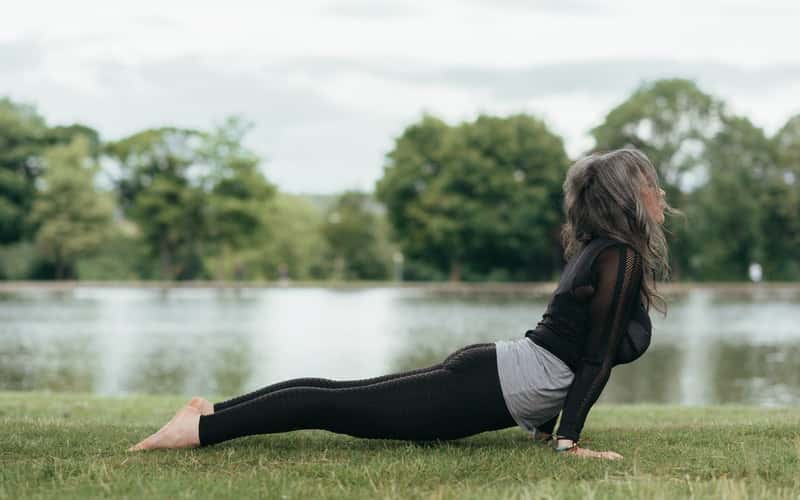 a woman doing yoga in the grass near a lake