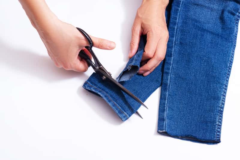 a woman cutting the hem off jeans
