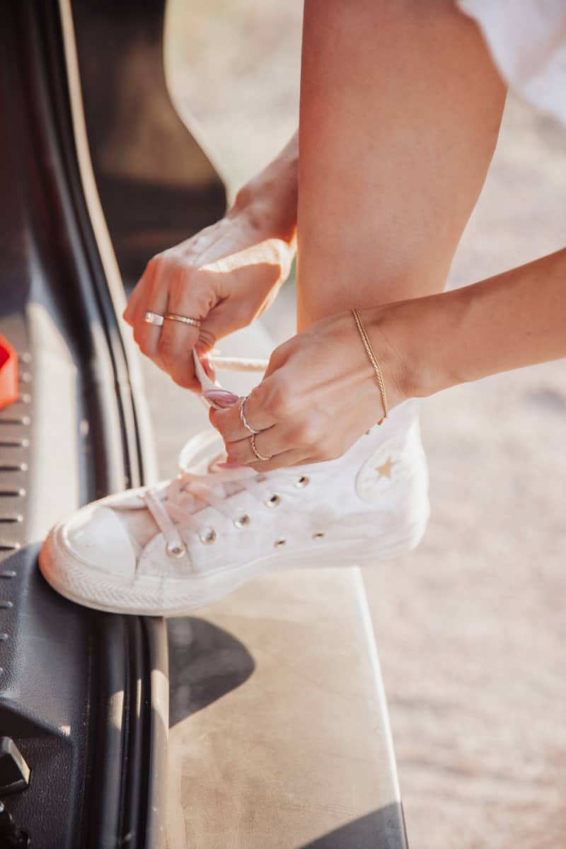 a woman tying shoelaces in a pair of white canvas shoes