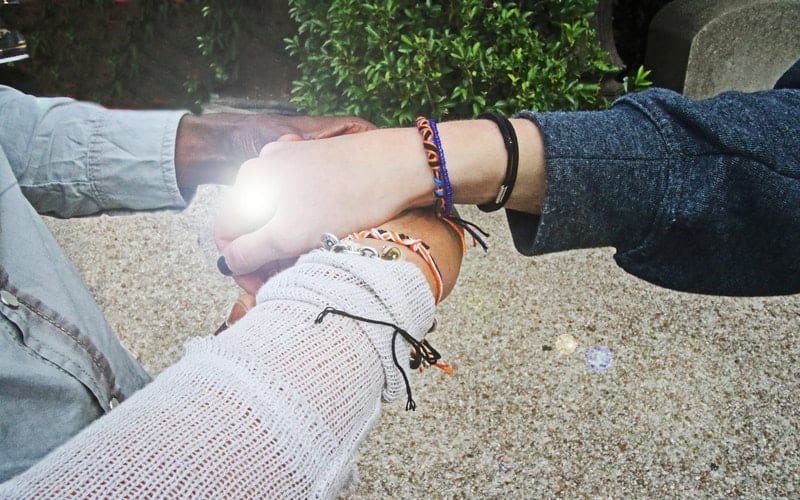 3 women wearing friendship bracelets holding hands