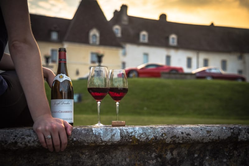 two glasses of wine sitting on a stone wall in front of a stately home