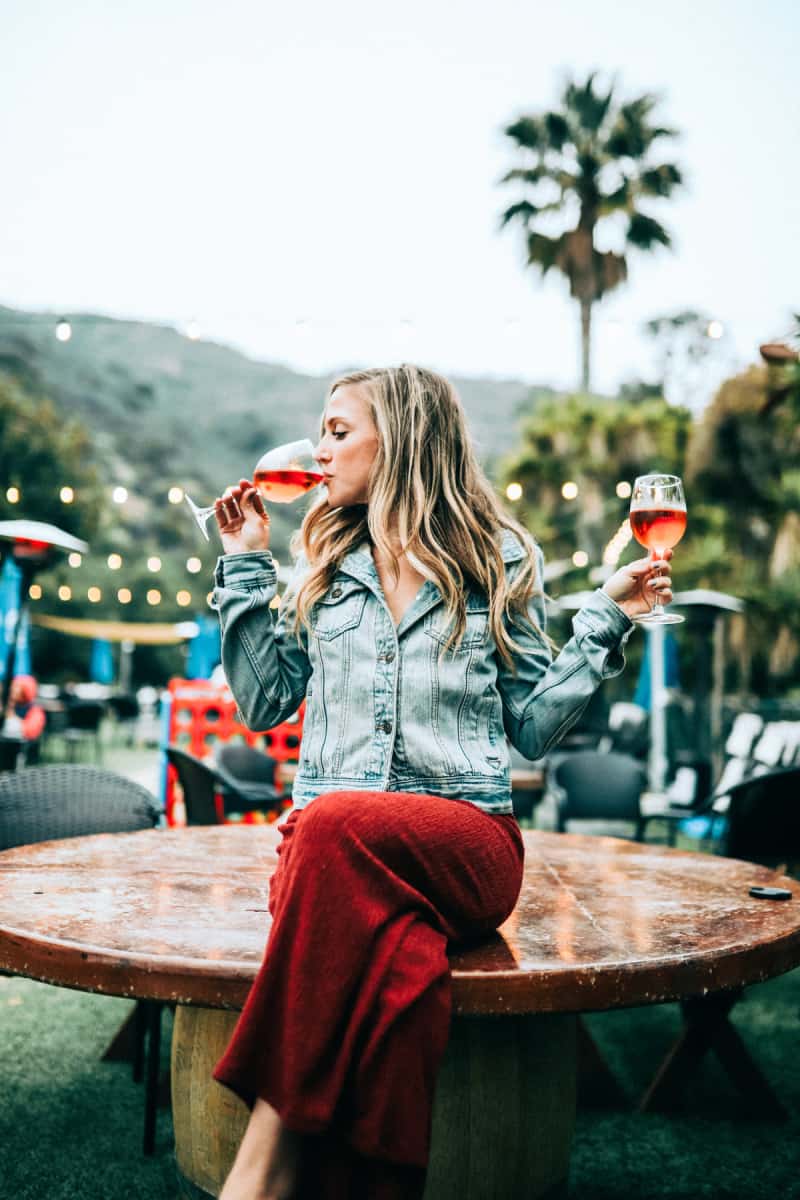 a woman wearing red pants and a denim jacket sipping wine