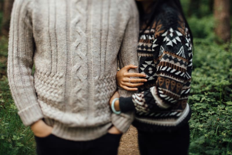 two people wearing sweaters standing in the woods