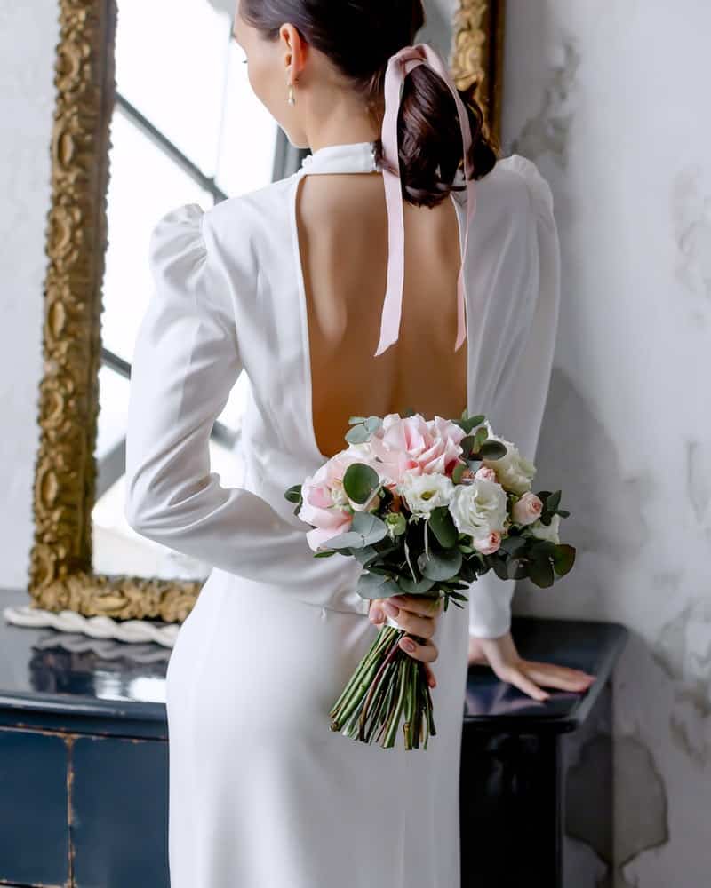 a woman wearing a white dress with a low ponytail tied with a pink bow