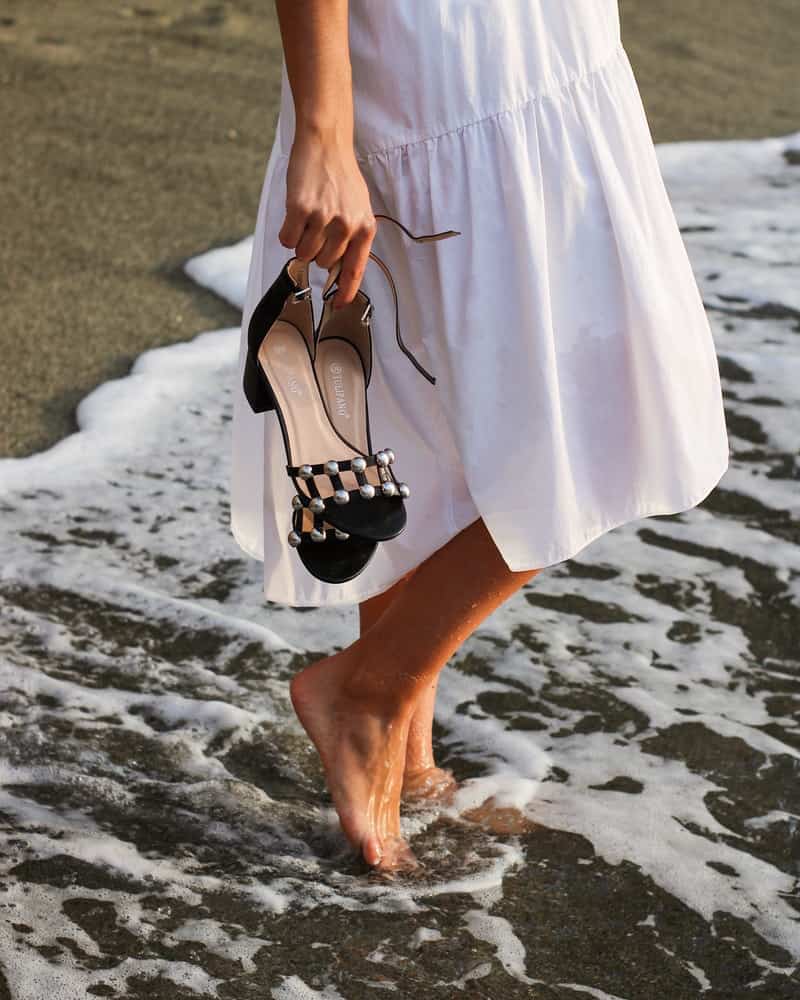 a woman wearing a white dress and holding black sandals