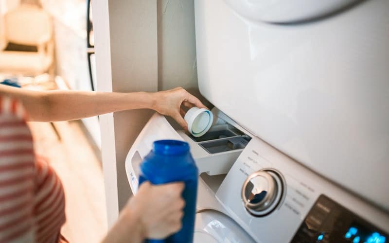 a woman adding laundry detergent to the washing machine