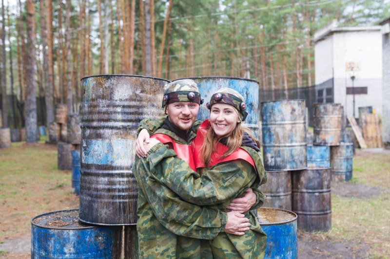 Smiling young man and woman posing with paintball markers outdoors.