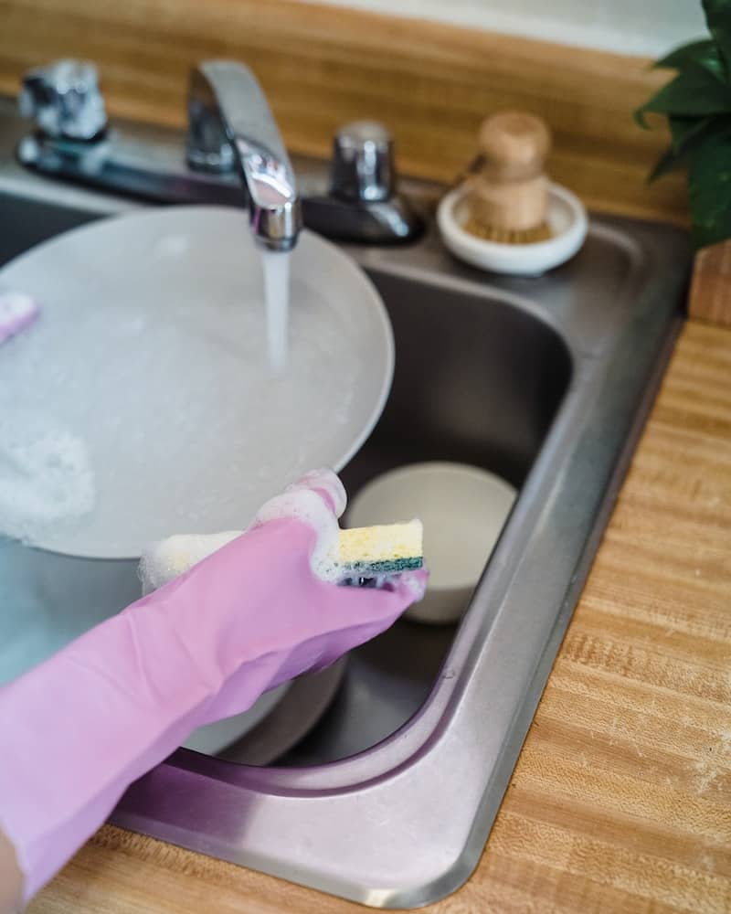 a woman washing dishes wearing gloves