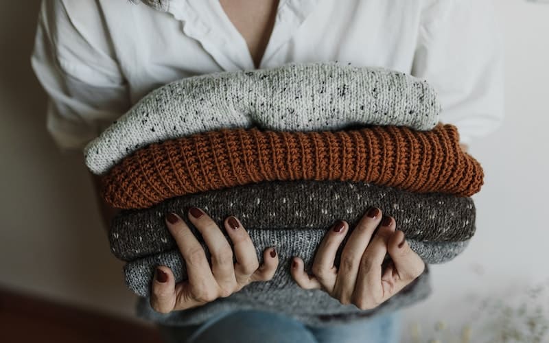a woman holding neatly folded sweaters