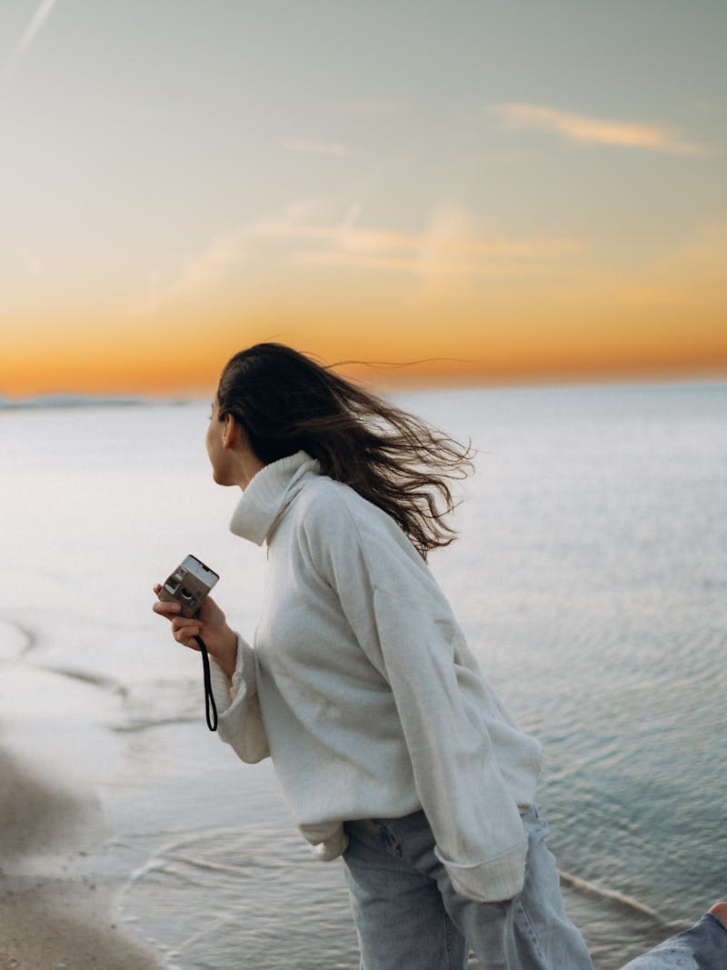 woman on the beach wearing a white turtleneck and jeans